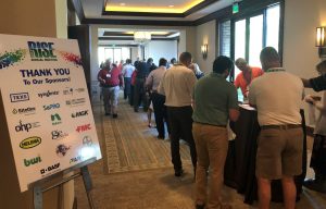 A large sign that says "Thank You To Our Sponsors" rests on an easel near people gathered around a long table indoors.